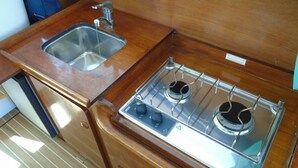 A compact kitchenette with a stainless steel sink and a gas stove with four burners. - Bateau à Quai (Sainte-Maxime)