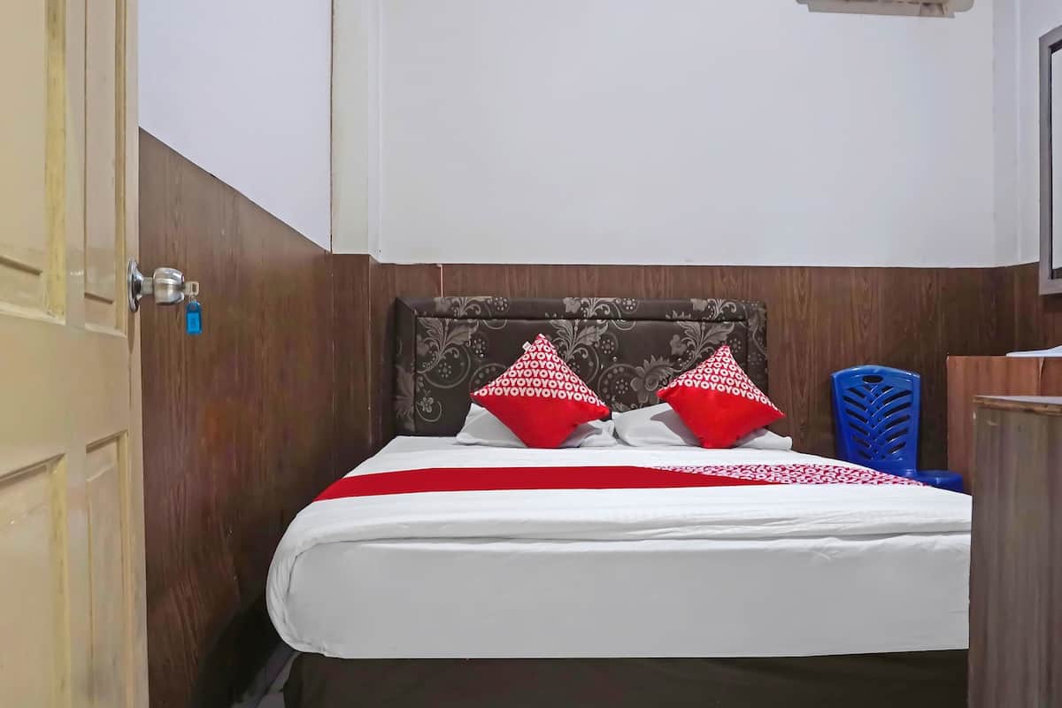 A hotel room with a bed, two red pillows, a white bedspread, and a wooden headboard.