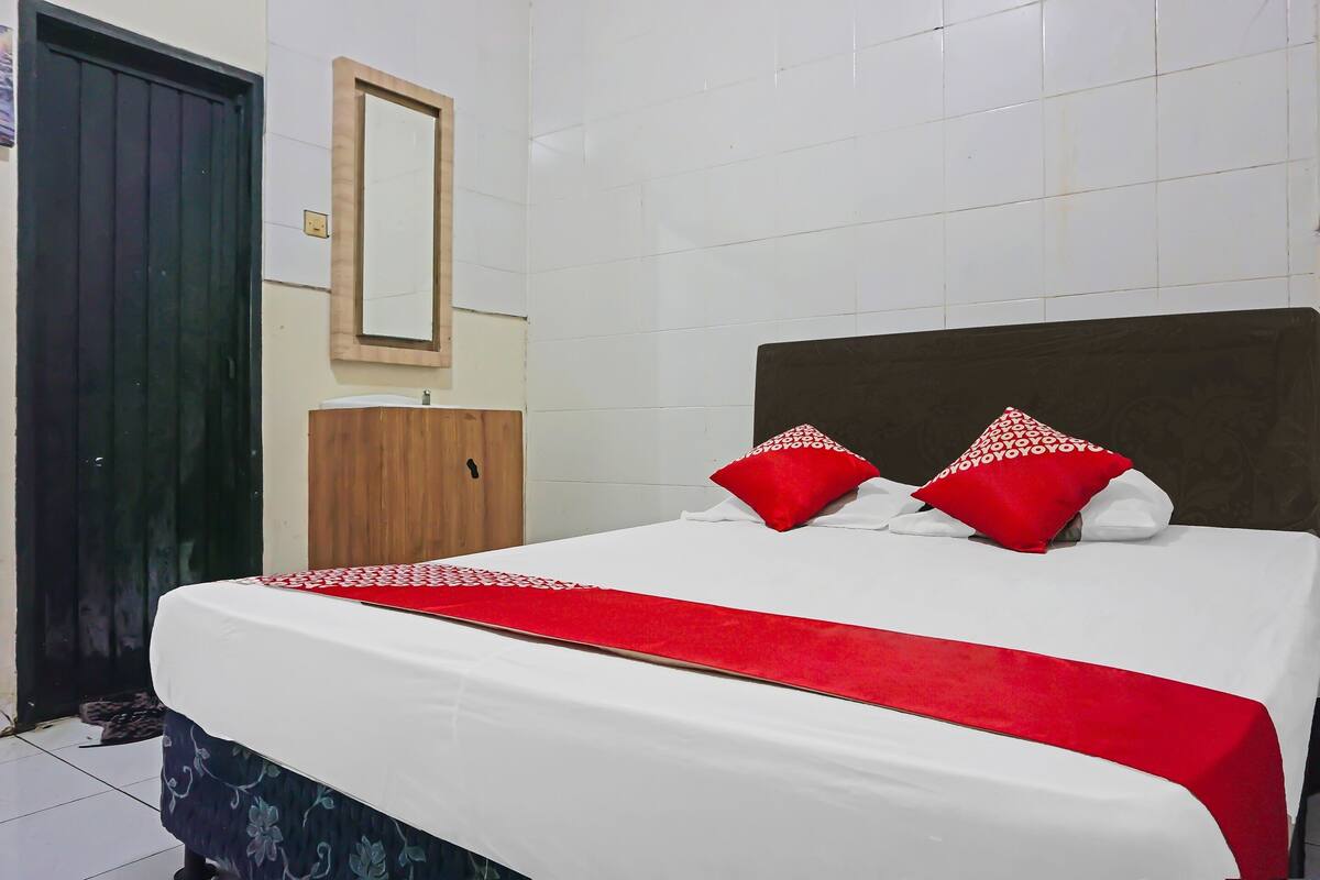 A neatly made bed with a red and white bedspread, two red pillows, and a wooden headboard.