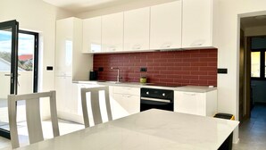 A modern kitchen with white cabinets, a red brick backsplash, and a dining area with a white table and chairs. - Penthouse apartment (Šimuni)