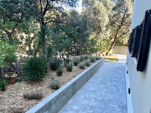A paved pathway leading to a building with a white exterior and black window shutters. - Garden Studio Apartment (Šimuni)