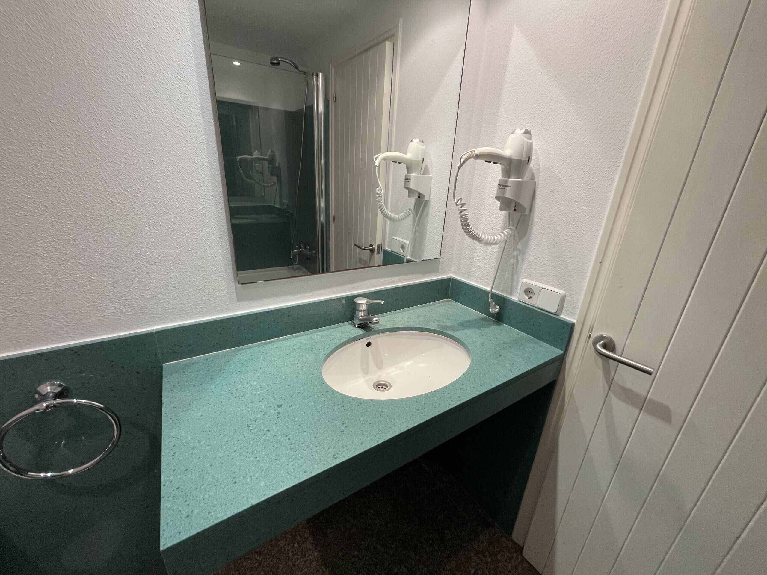 Un baño con un lavamanos blanco, un espejo y un secador de pelo fijado en la pared.