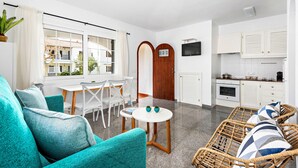 A bright, modern living room with a sofa, a dining table, and chairs. There is a kitchen area with cabinets and a TV. - Apartment SON BOU, 67 (Son Bou)