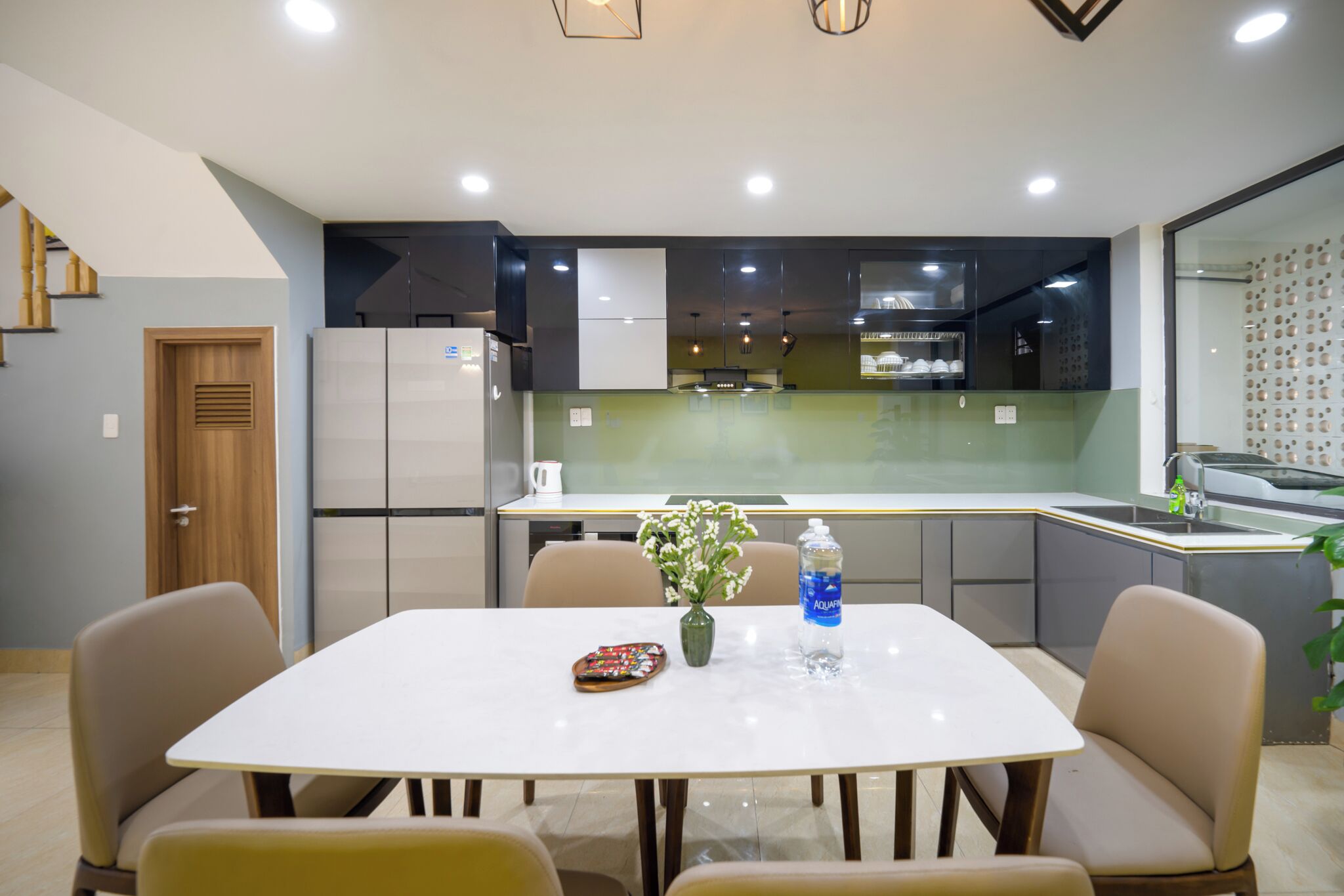 Een moderne keuken met witte kasten, een inbouwoven en een eethoek met een witte tafel en stoelen.