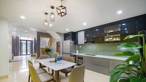 A modern kitchen with a dining area, featuring a large island, stainless steel appliances, and a staircase leading to an upper level. - N to M House (Da Nang)