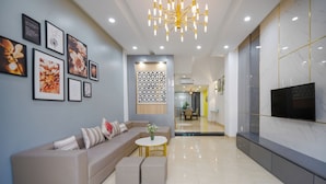 A modern living room with a beige sofa, a round coffee table, and a TV mounted on the wall. - N to M House (Da Nang)