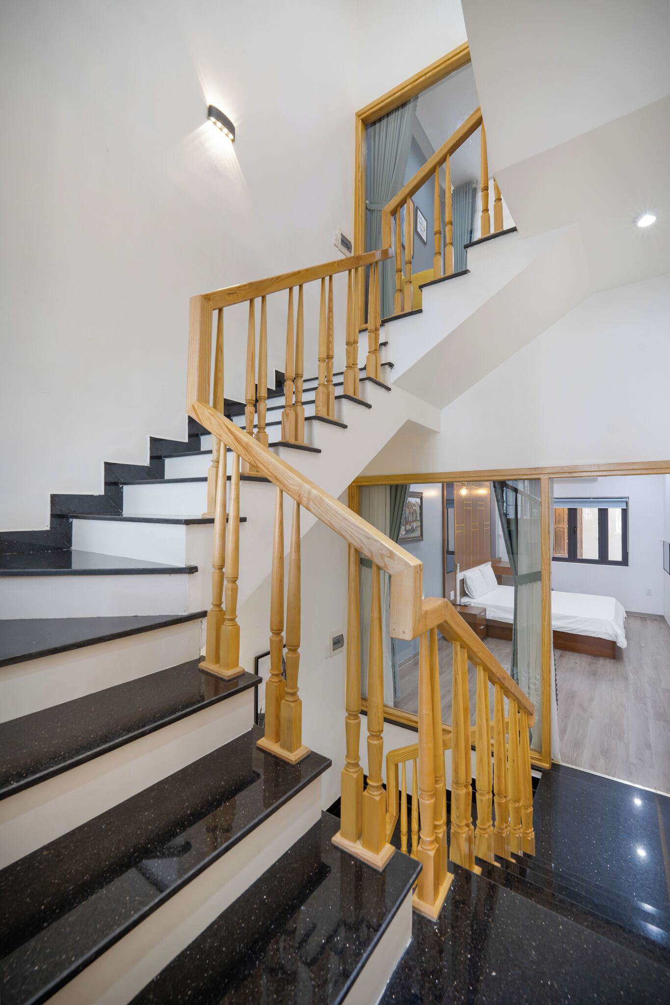 A staircase with black steps and wooden balusters, leading to a bedroom with a bed and a window.