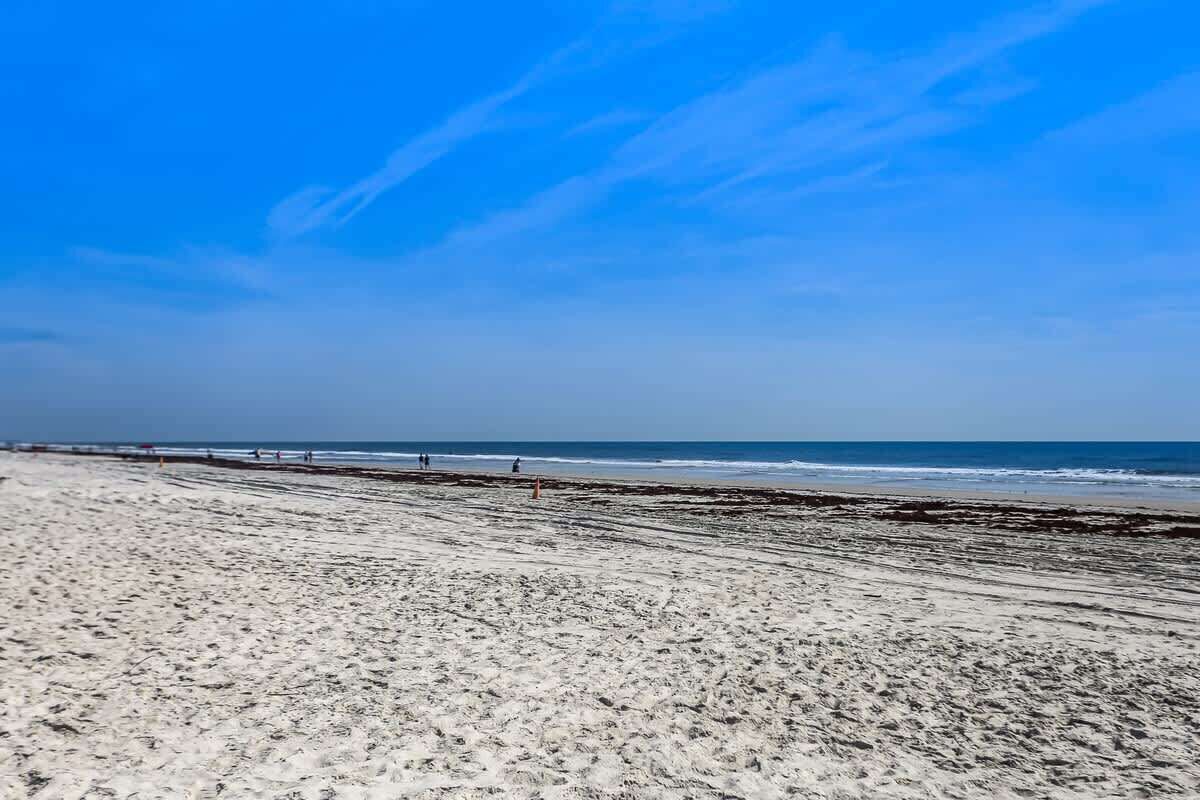 A wide sandy beach with a clear blue sky and calm sea.