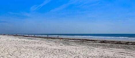 A wide sandy beach with a clear blue sky and calm sea.