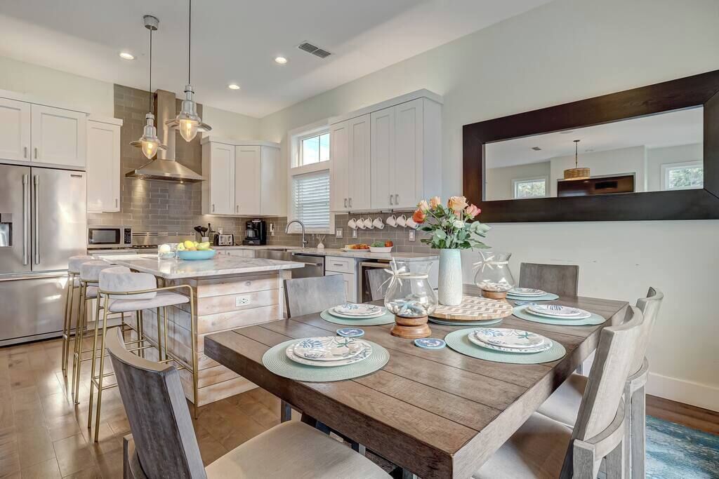 A modern kitchen with white cabinets, stainless steel appliances, and a wooden dining table set for four.