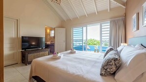 Een hotelkamer met een groot bed, een televisie, een balkon met uitzicht op zee en een badkamer met een spiegel en wastafel.