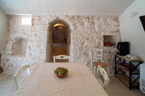 Un coin repas aux murs de pierre, avec une table dressée pour deux personnes, une petite cheminée et un téléviseur posé sur un meuble en bois.
