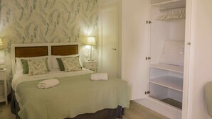 Ein ordentlich bezogenes Bett mit grüner Bettdecke und Kissen, eine Nachttischlampe und ein Kleiderschrank mit Platz zum Aufhängen.