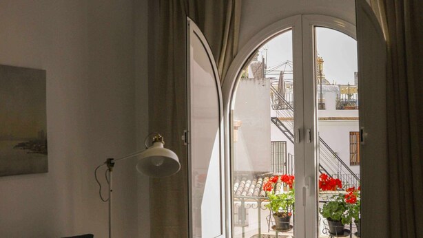 Ein Wohnzimmer mit einer Couch, einem Glastisch, einer Stehlampe und Blick durch ein großes, mit Vorhängen drapiertes Fenster.