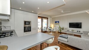 Una cocina moderna con armarios blancos, horno integrado y zona de comedor con mesa y sillas.