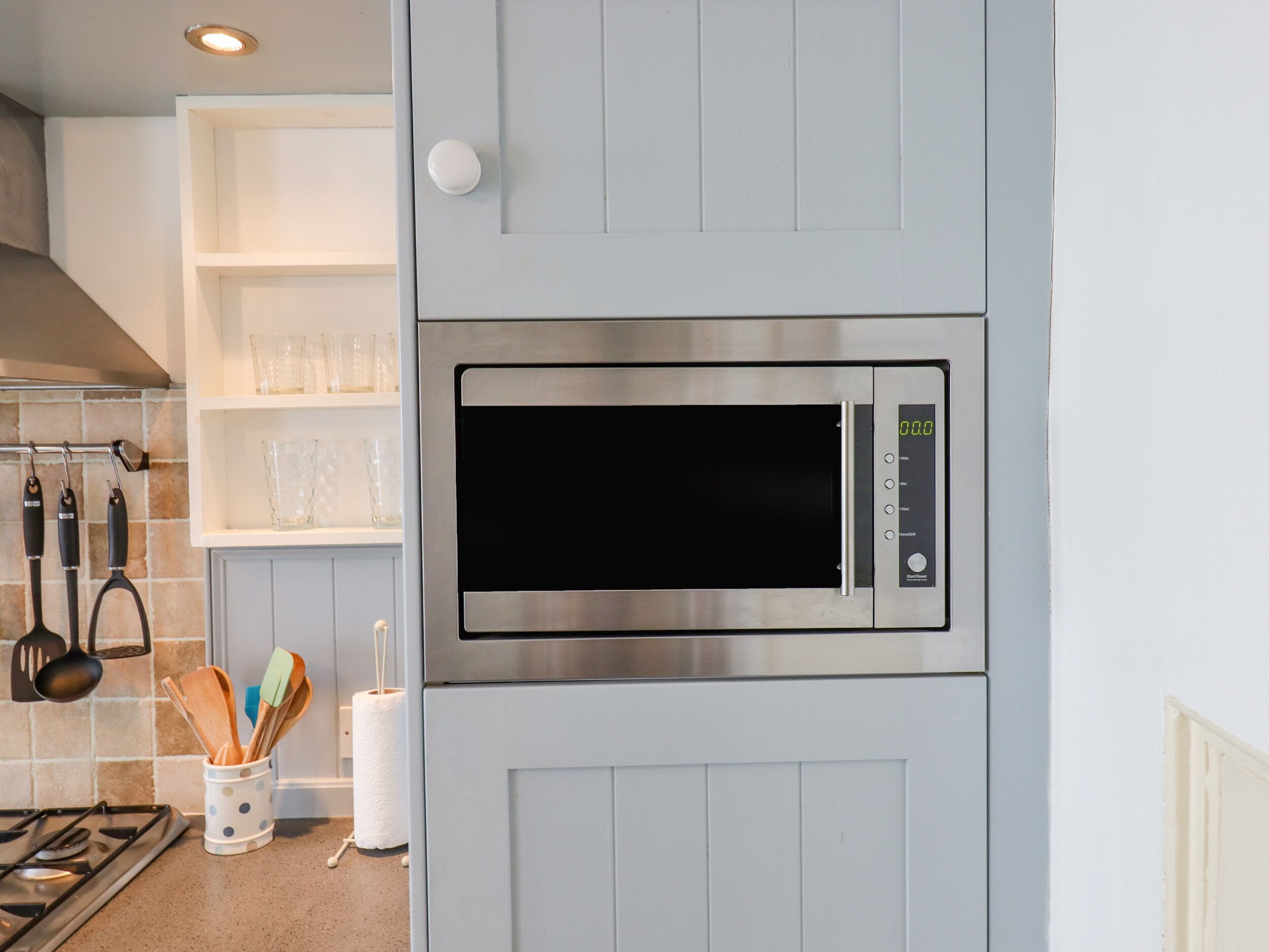 Une cuisine équipée d’un four à micro-ondes encastré, d’une cuisinière à gaz et d’un meuble blanc doté d’une poignée.