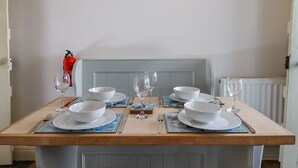 Una mesa de comedor dispuesta con cuencos, platos y cubiertos blancos, con un extintor y un cuadro en la pared.