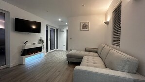Ein modernes Wohnzimmer mit einem grauen Ecksofa, einem Flachbildfernseher an der Wand und einem Kamin mit Glastür.