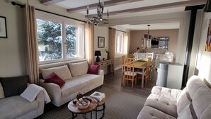 Een gezellige woonkamer met een bank, een eettafel met stoelen en een keuken op de achtergrond.