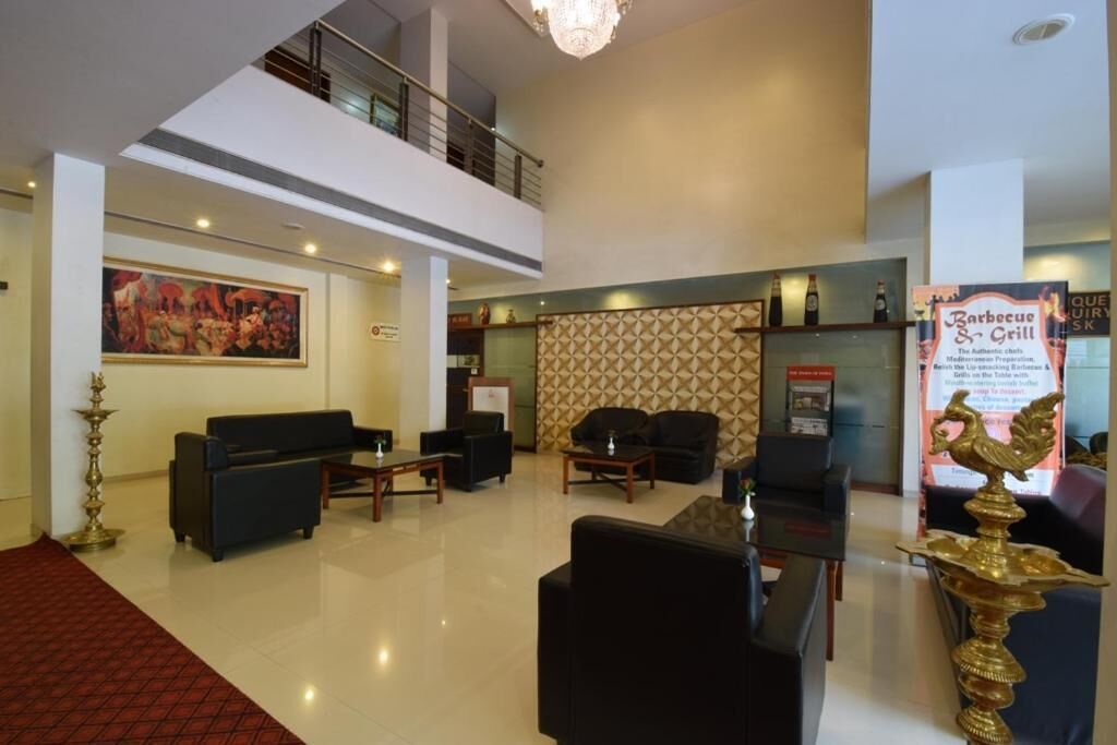 A lobby with a high ceiling, a staircase, a seating area with sofas and tables, a decorative wall, and a sign for a barbecue and grill.