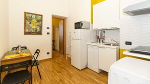 A compact kitchen with a microwave, refrigerator, and dishwasher. There's a dining table with chairs and a painting on the wall. - GuestHost - Porta Nuova Mini Flat 2 New! (Torino)