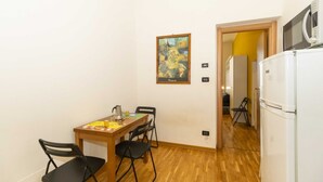 A small kitchen with a dining table, chairs, a refrigerator, and a painting on the wall. - GuestHost - Porta Nuova Mini Flat 2 New! (Torino)