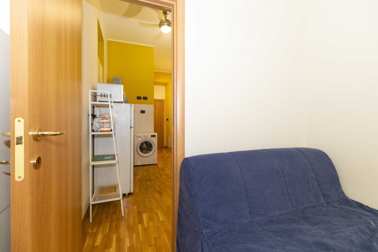 A room with a bed, a washing machine, and a shelf with laundry items.