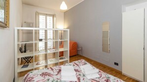 Un dormitorio con cama, armario blanco, estantería, ventana y radiador.