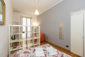 Une chambre à coucher avec un lit, une armoire blanche, une bibliothèque, une fenêtre et un radiateur.