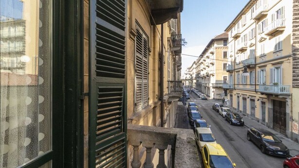 Una calle estrecha con coches aparcados y edificios con balcones.