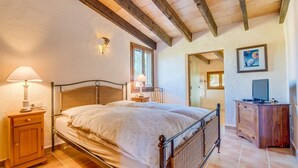 A bedroom with a bed, bedside lamps, a wooden cabinet, and a television. - Finca Ferragut - Beautiful Mallorcan finca with pool (main house) (Artá)