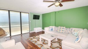 A living room with a white sofa, a coffee table, a ceiling fan, and a view of the beach. - Sand Dollar 1-504 - 5th Floor Ocean Front Condo in St. Augustine! (St. Augustine)