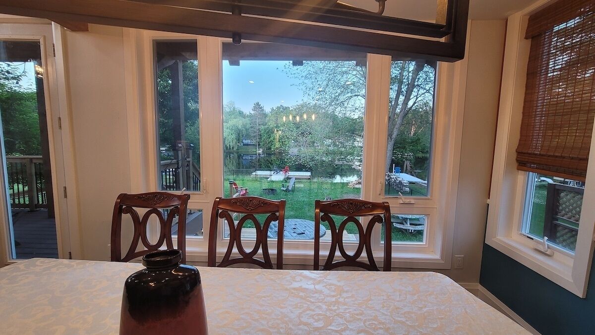 A dining area with a table and chairs, large windows with a view of a backyard, and a chandelier.