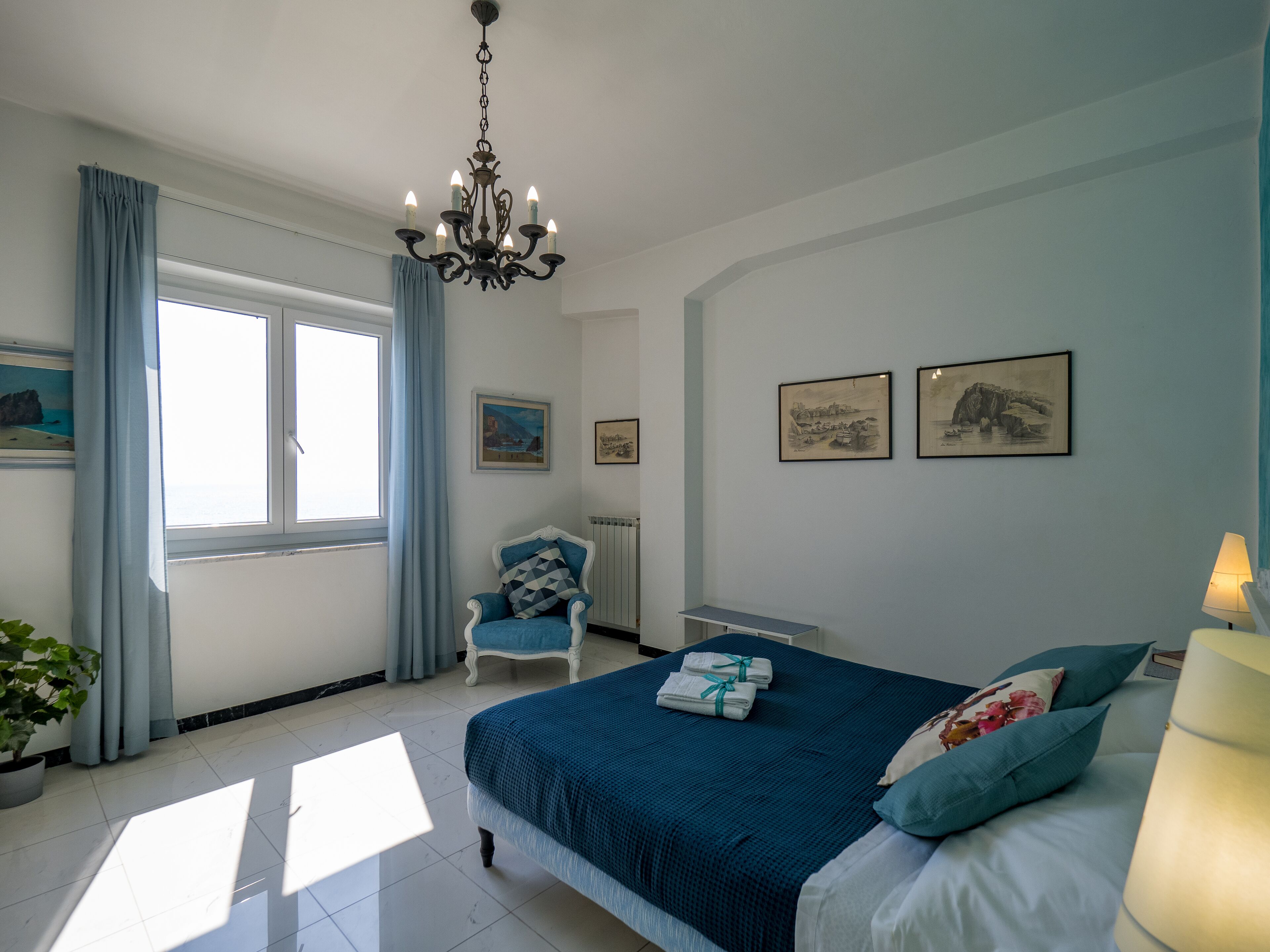 A bedroom with a bed, a chair, a table, and a chandelier.