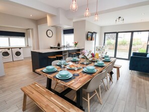 A modern kitchen with a central island, built-in appliances, and a dining area with a wooden table set for six. - Tan Y Fron (Llandudno)