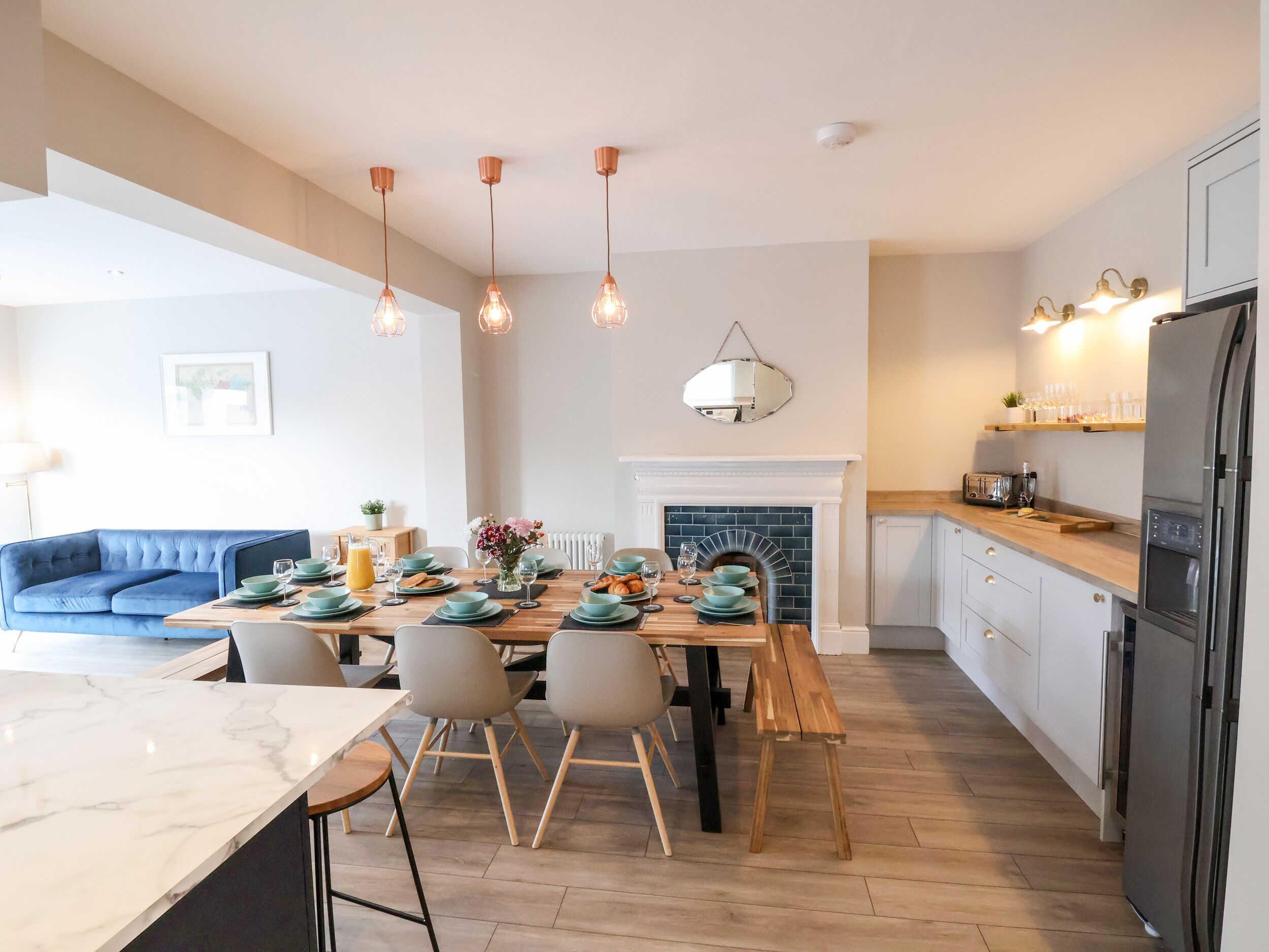 A modern kitchen with a dining area, featuring a wooden table, chairs, and a blue sofa.