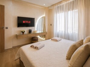 Ein Hotelzimmer mit Bett, Wand-Fernseher, Nachttisch mit Lampe und einem Fenster mit Vorhängen.