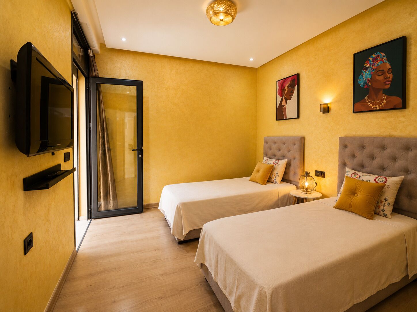 A hotel room with two beds, a TV, a door, and artwork on the wall.