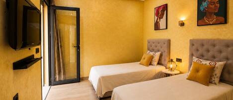 A hotel room with two beds, a TV, a door, and artwork on the wall.