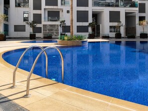 A modern hotel with a swimming pool, a palm tree, and a building with large windows. - Loli Home Agadir - Bay Premium Pool (Agadir)