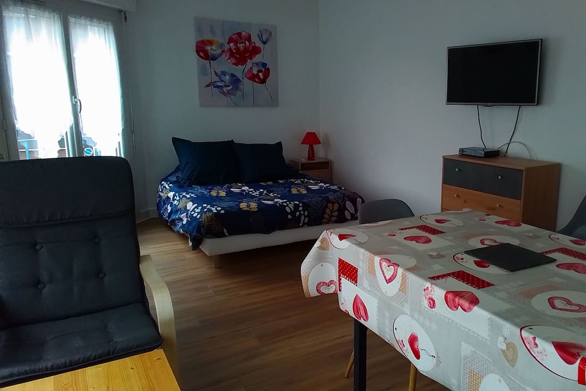 A bedroom with a bed, bedside table, lamp, TV, and a table with a heart-patterned tablecloth.