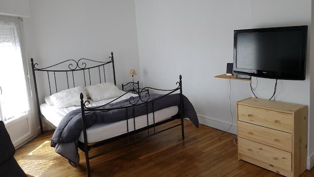A bedroom with a bed, a wooden dresser, and a television mounted on the wall. - Franglais flats (Boulogne-sur-Mer)