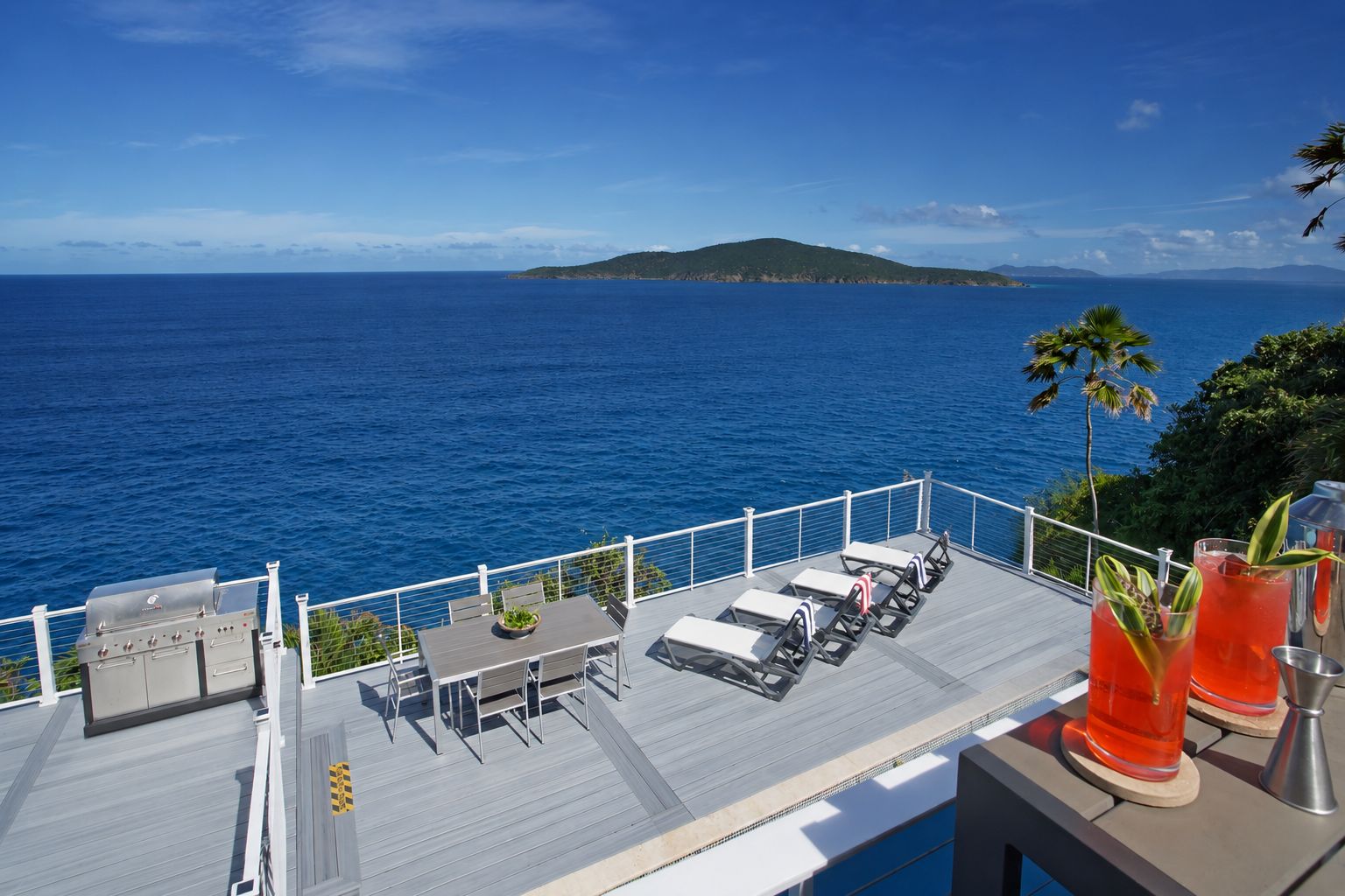 Um deck com área de estar externa e churrasqueira, com vista para um corpo d'água e uma ilha ao longe.