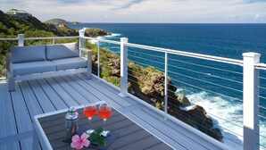 Una terrazza con ringhiera bianca, un divano e un tavolo con due bicchieri di bevanda rossa e un fiore.