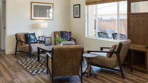 En stue med trægulv, en sofa, et sofabord og et vindue med udsigt til et træhegn.