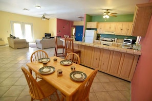 Un comedor con una mesa de madera dispuesta para cuatro, una cocina con armarios de madera y una sala de estar con sofá y televisor.