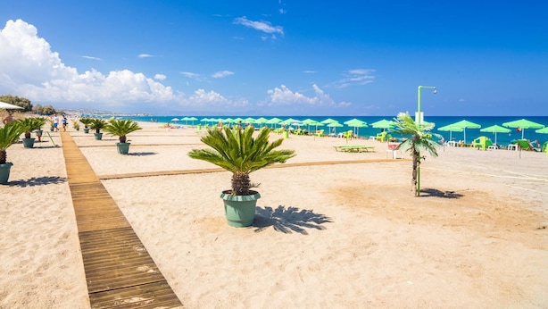 A beach with a wooden walkway, green umbrellas, and palm trees.