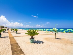 A beach with a wooden walkway, green umbrellas, and palm trees. - Konstantin Apartment - Rethymno (Rethymno)