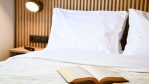 A neatly made bed with white linens, a bedside table with a lamp, and an open book on the bed.