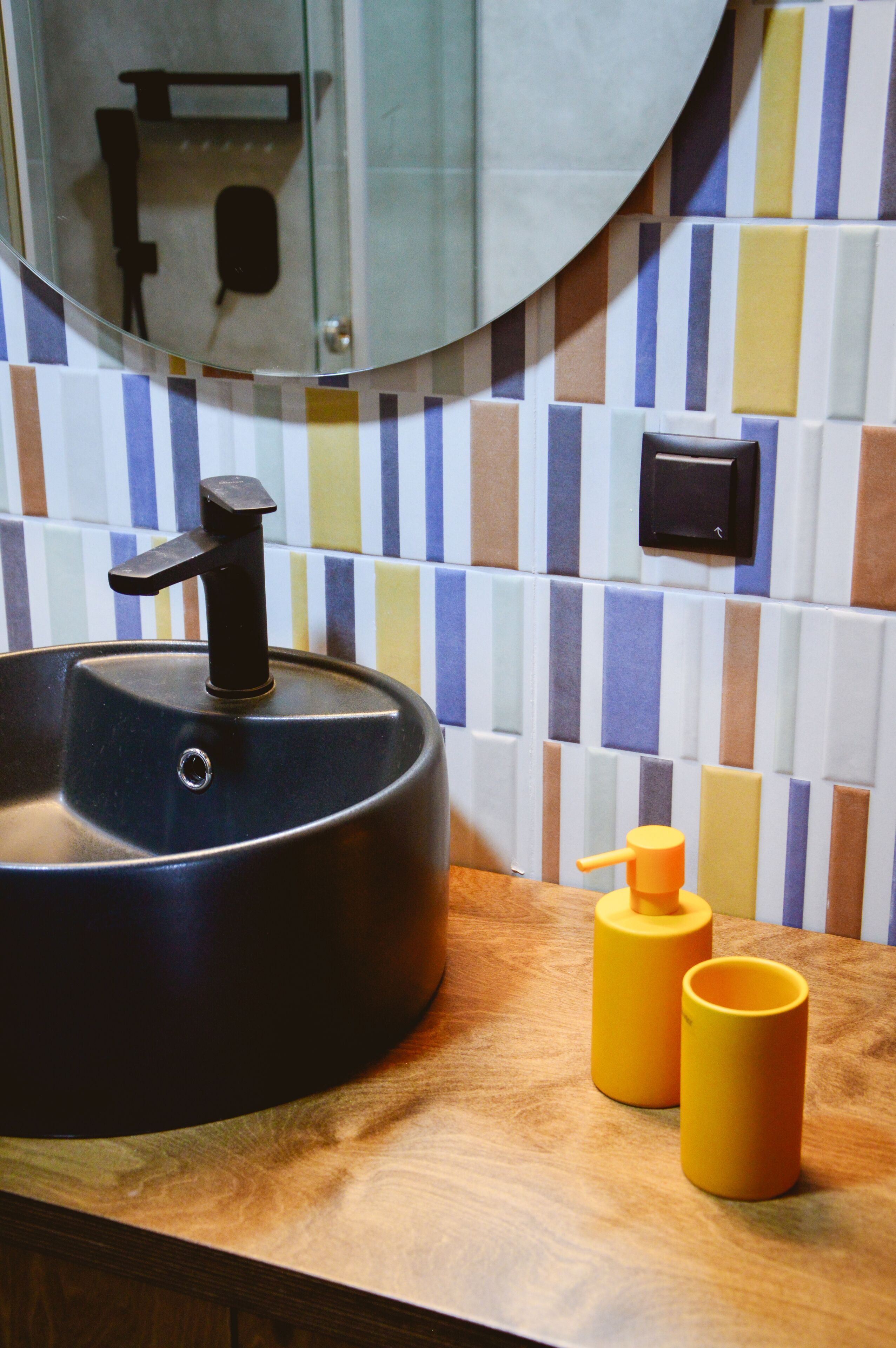A bathroom with a round sink, a mirror, and a tiled wall.